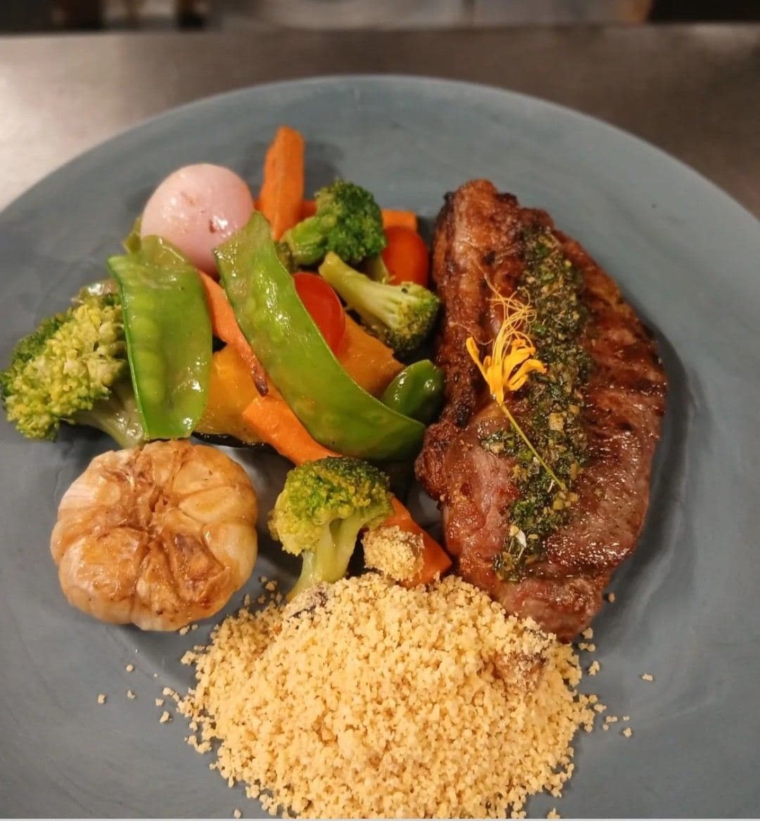 Grilled steak with mixed vegetables, roasted garlic, couscous, and herbs