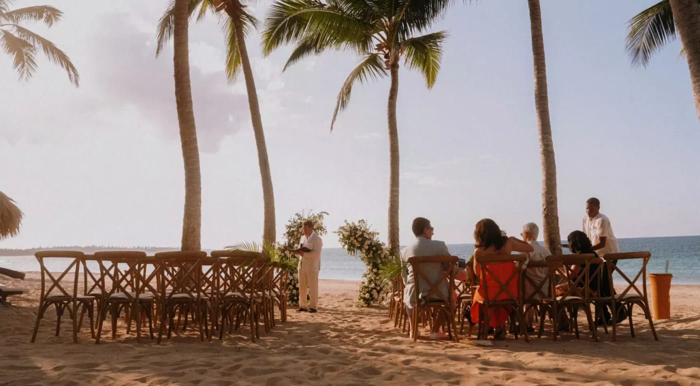 Outdoor beachfront dining setup with guests seated at tables under palm trees.