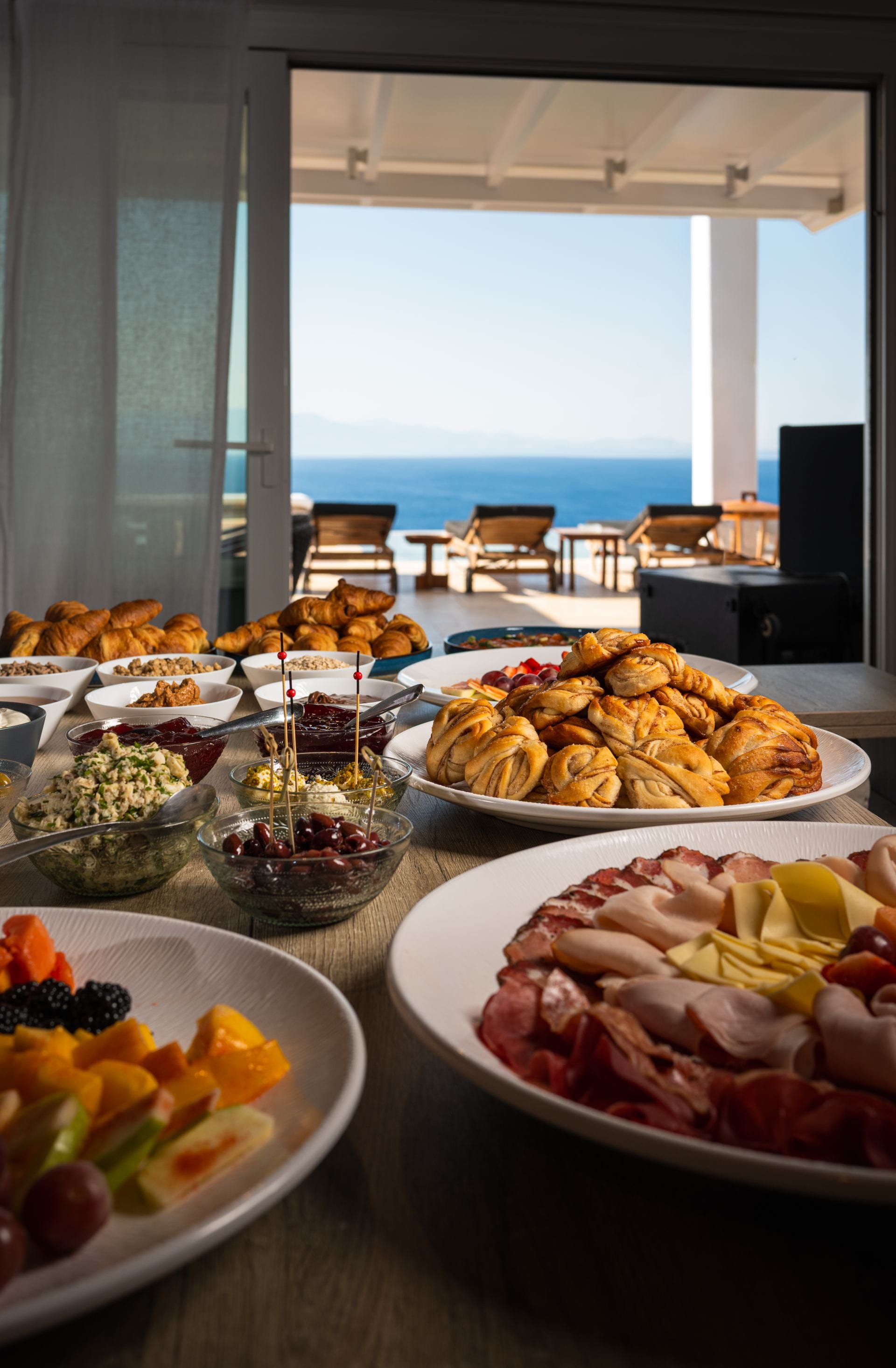 Luxury breakfast spread with fresh pastries, fruit and charcuterie overlooking the sea.
