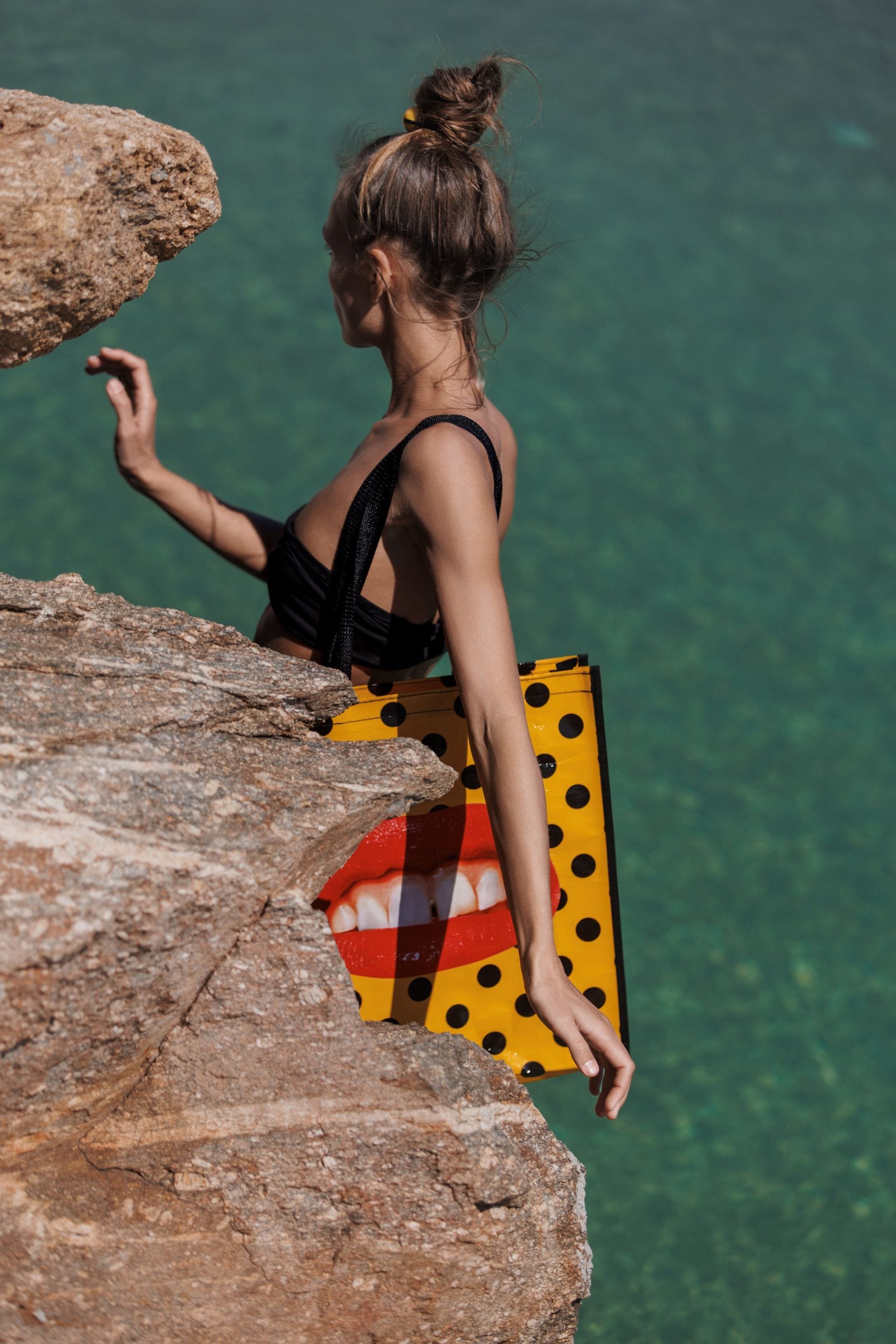Woman carrying a colourful statement bag beside crystal clear turquoise water.